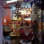 A shop window showcasing festive decorations for the Marianna Black Library Used Book Store, featuring snowflake ornaments, Santa cutouts, and vibrant holiday colors.